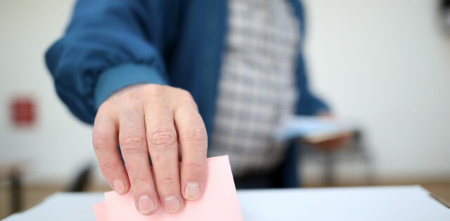 Man casts his ballot as he votes for the local elections at a polling station. Focus on hand.