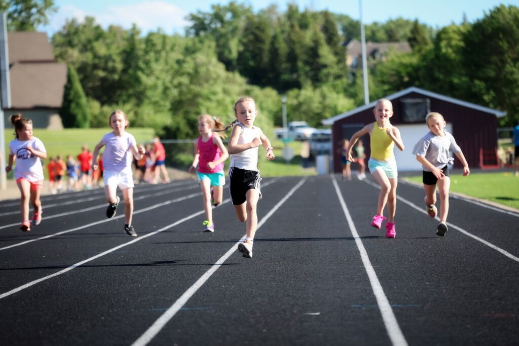 Youth programs: Girls running on a track in a youth track and field event, promoting fitness and healthy competition.