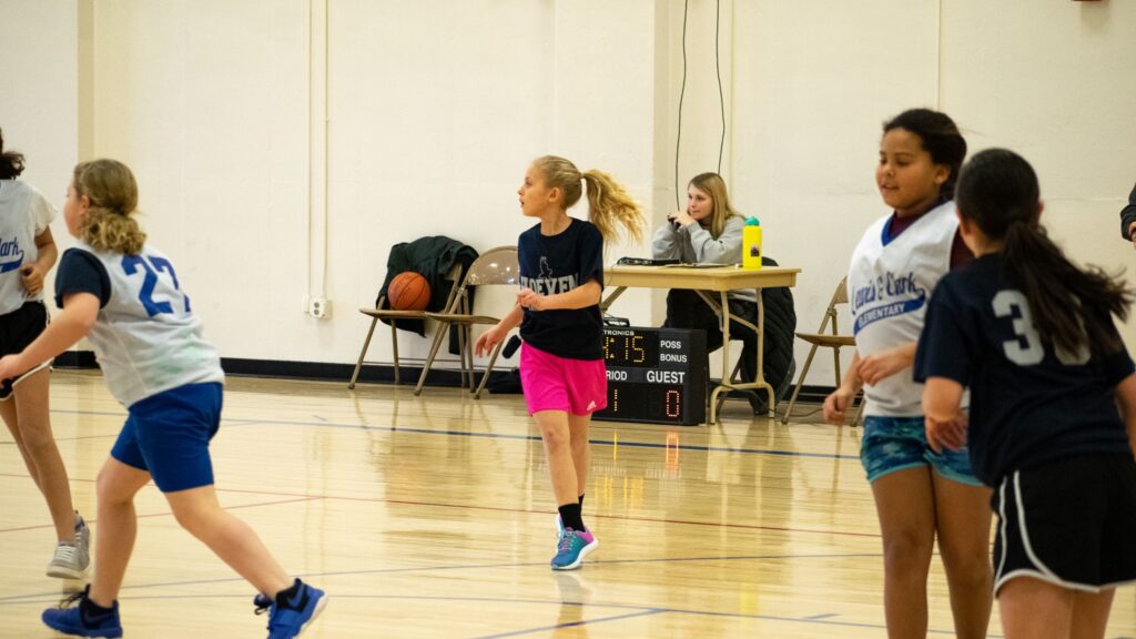 A young basketball player in mid-motion, dribbling a basketball on an indoor court during a youth league game.