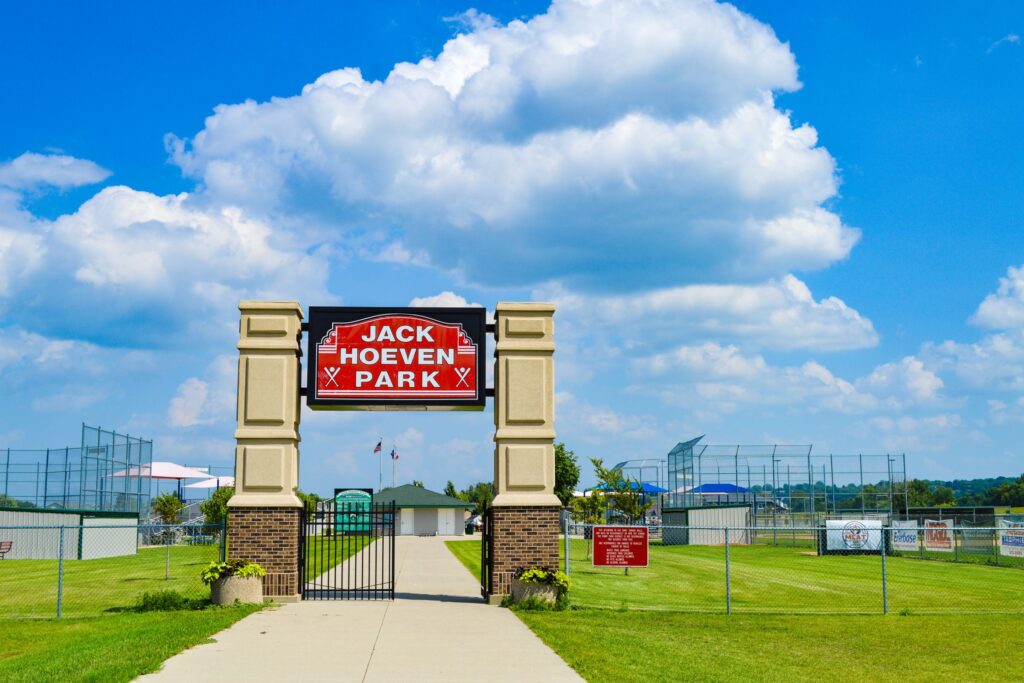 Entrance to Jack Hoeven Park, a baseball and softball complex with 4 diamonds. Green grass, blue sky, white clouds, a beautiful summer day for sports.