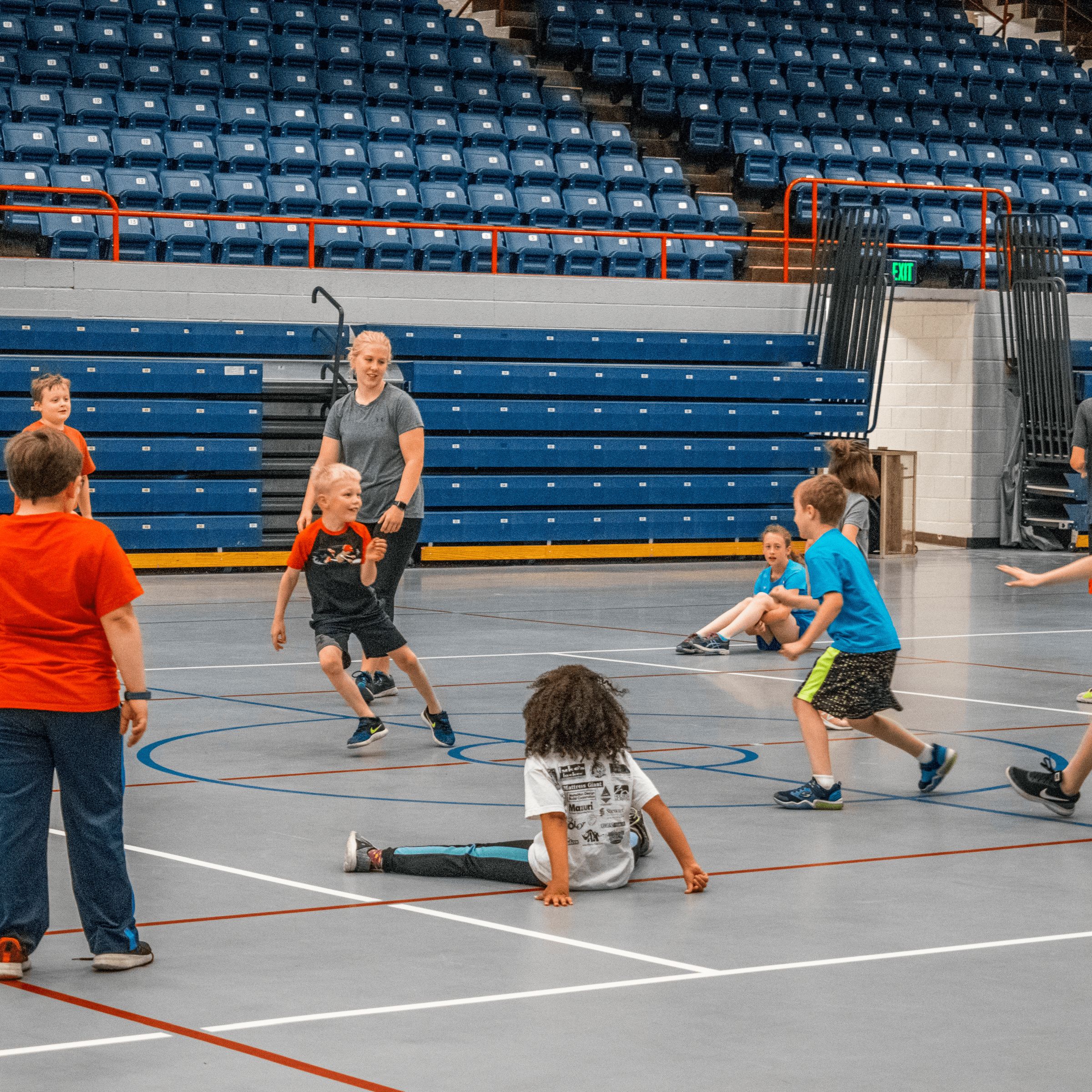A large group of children participating in an organized game in a gymnasium, with several kids running and playing together during a fitness session.
