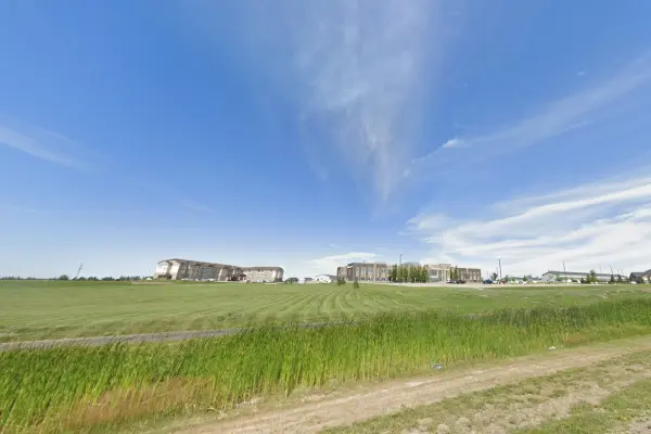 A paved trail trail next to a large mowed open space under a blue sky with wispy clouds.