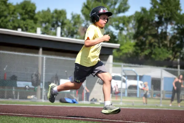 Boy in helmet and yellow shirt runs on baseball field during daytime.