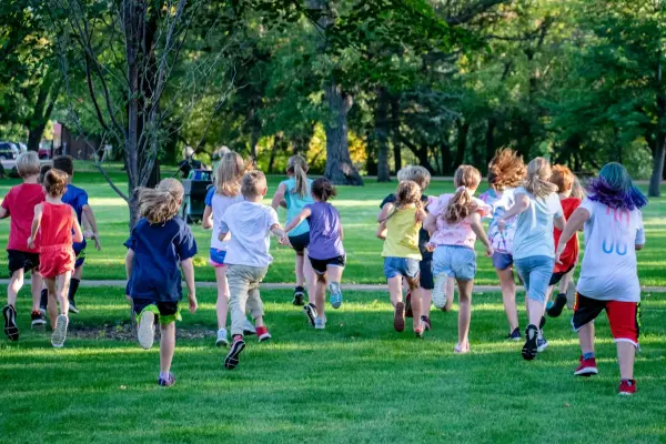 A large group of children running across a grassy field at the start of a cross-country race at a local park.