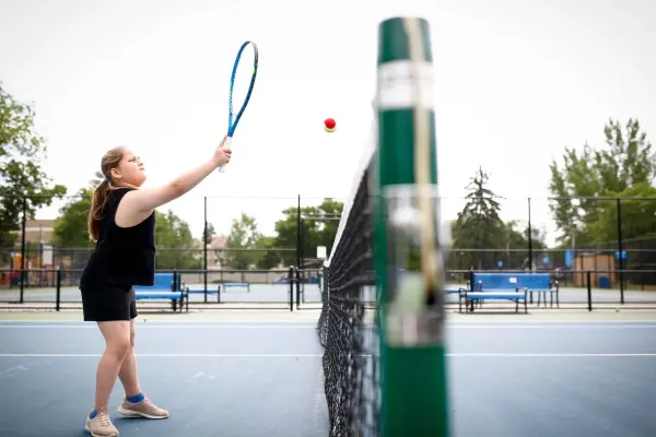 A young girl plays a shot close to the net at a blue outdoor tennis court.