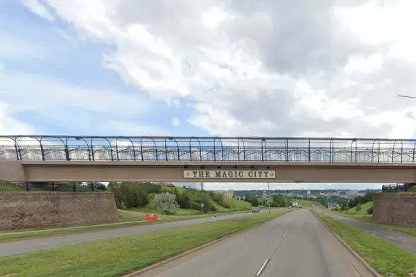 Screenshot of Google Map view of the N Broadway – 21st Ave NW trail in Minot, ND. A path next to a 4-lane road with downward slope under a walking bridge with a sign that reads "The Magic City."