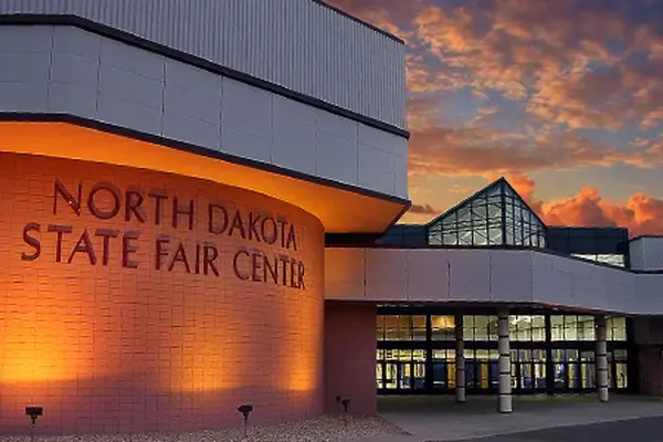 North Dakota State Fair Center building exterior illuminated at sunset with a dramatic orange and purple sky.