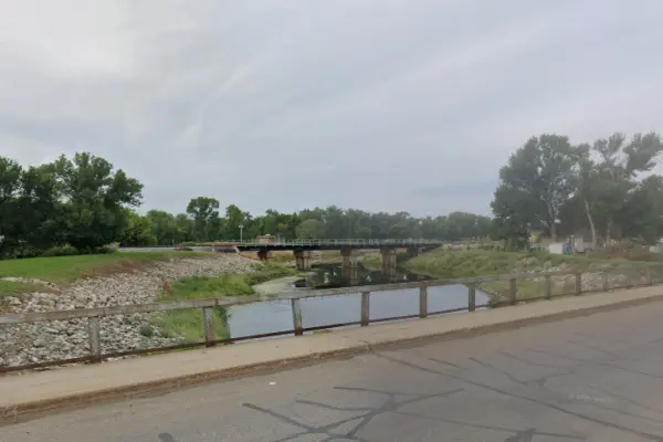Screenshot of Google Map view of the Oak Park – 16th Street SW trail in Minot, ND. Sidewalk trail that passes over a narrow river with a railroad bridge in the background.