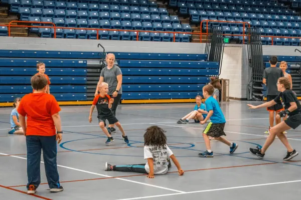 A large group of children participating in an organized game in a gymnasium, with several kids running and playing together during a fitness session.