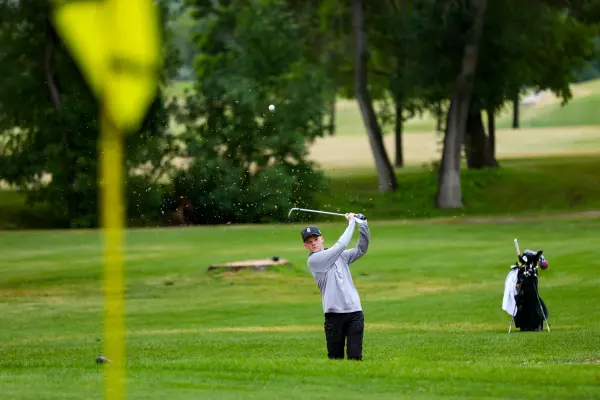 Golfer hitting out of a bunker on the course. Make a tee time and enjoy golfing. Golf course with trees in background.