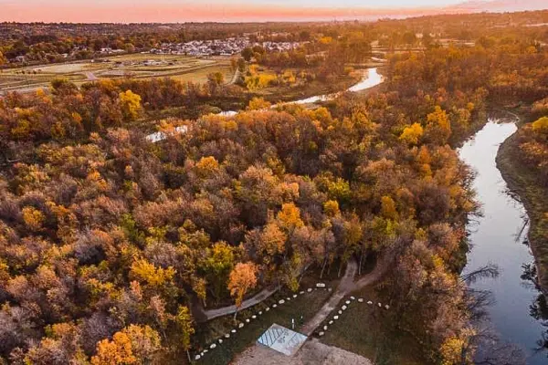 Aerial view of a winding river flowing through a dense woodland forest with autumn foliage at sunset.