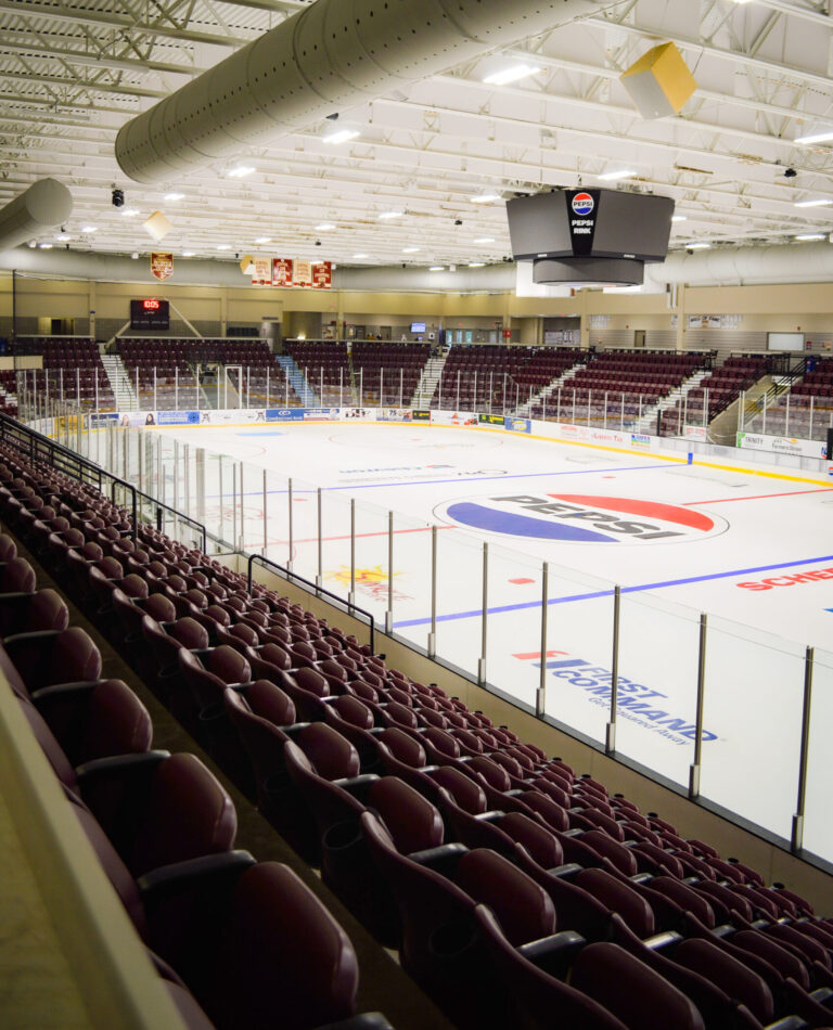 Empty Pepsi Rink ice hockey arena featuring rows of maroon stadium seats and a large Pepsi logo on the ice surface.